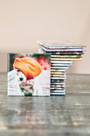 Stack of photo prints with a dog wearing an orange beanie on a wooden surface.