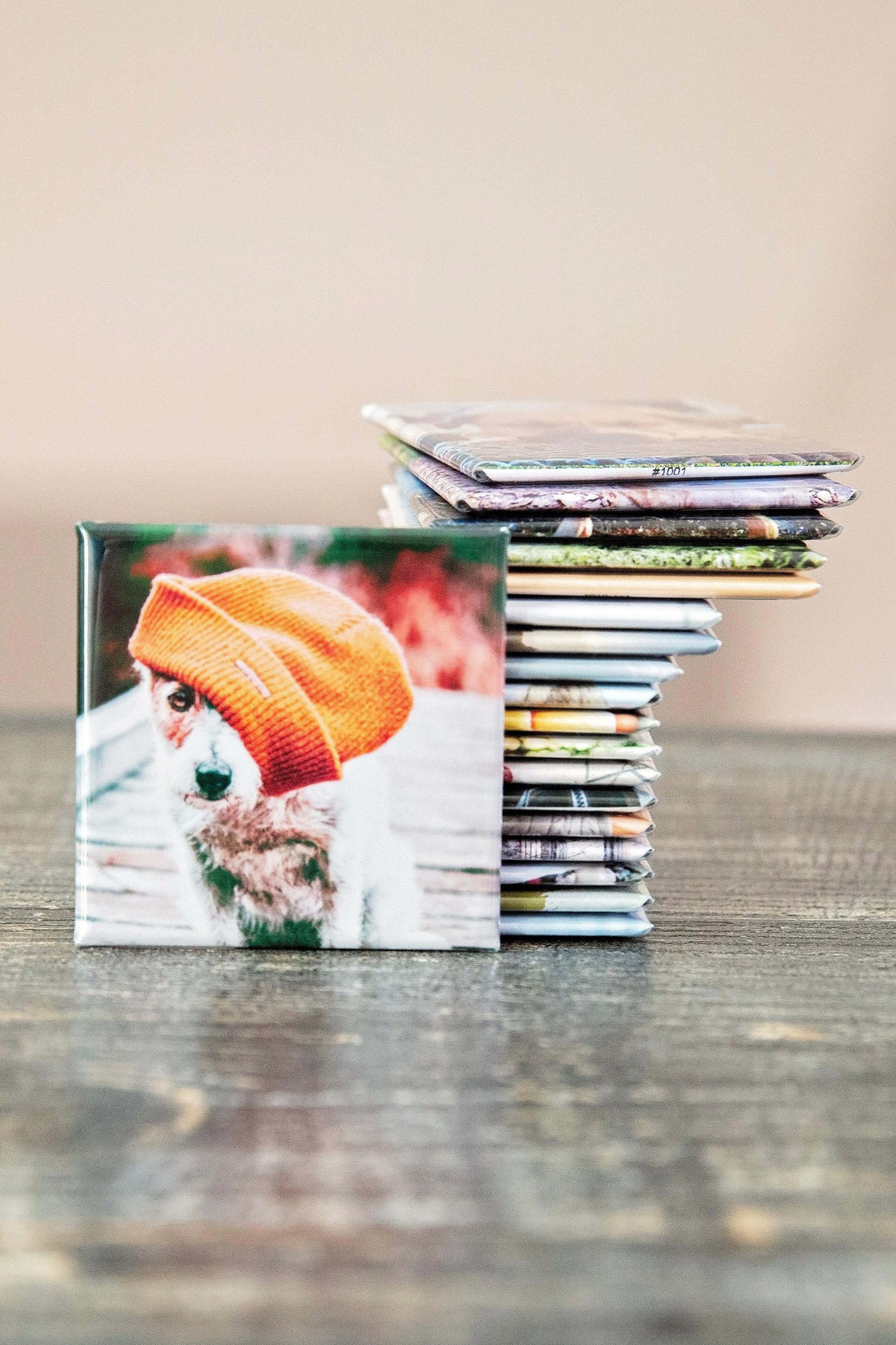 Stack of photo prints with a dog wearing an orange beanie on a wooden surface.
