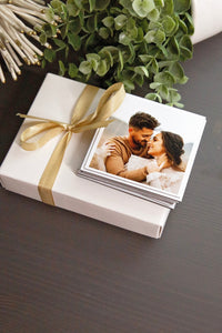 White gift box with a gold ribbon and photo of a couple on a dark surface with plants.
