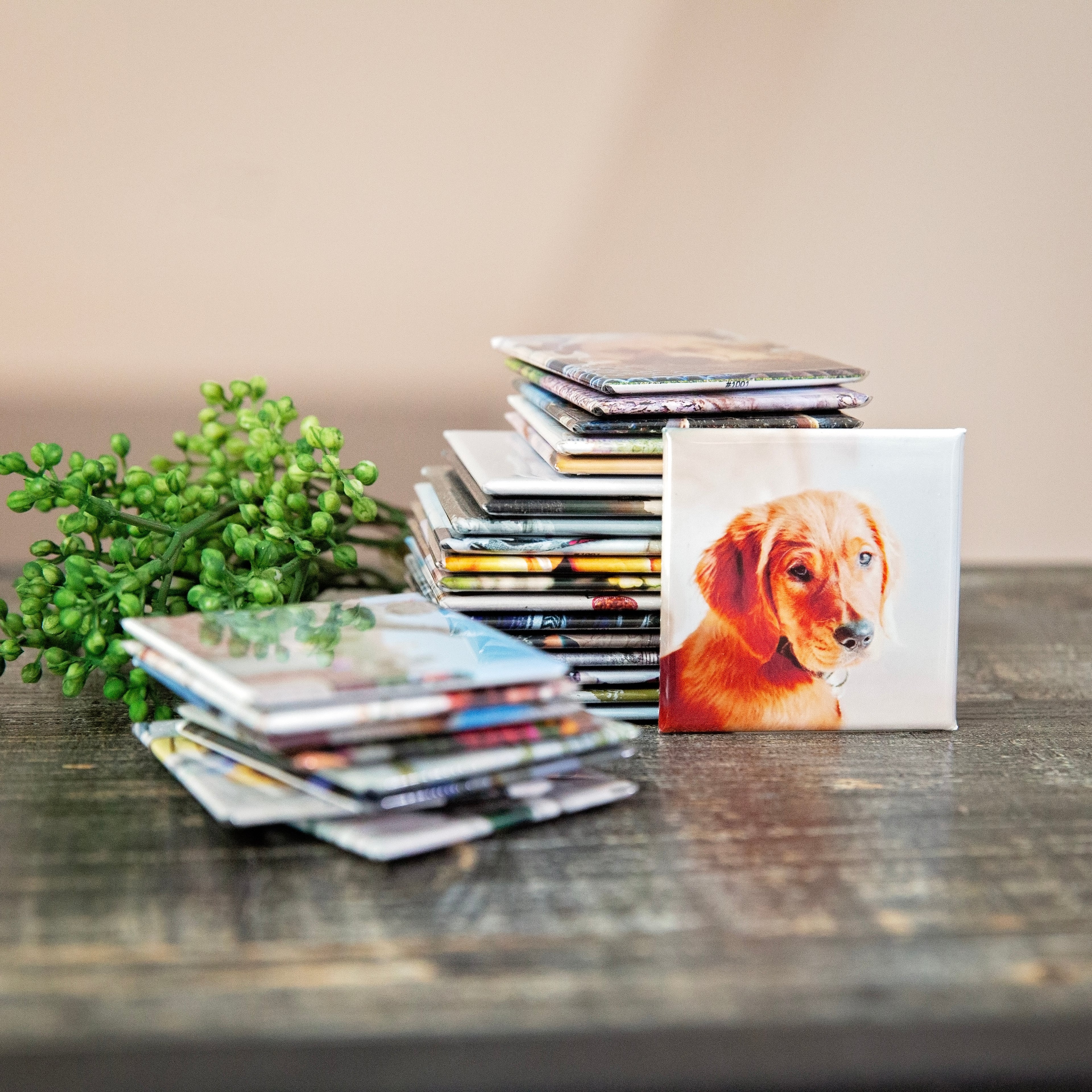 Custom pet photo magnet with dog, stacked with other personalized photo magnets on wooden background.